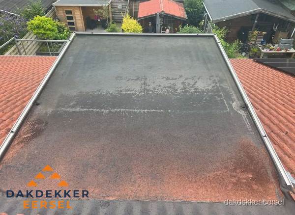 Verouderd plat dak met slijtage tussen schuine daken in Eersel