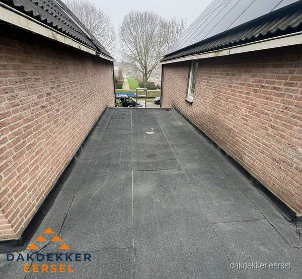 Plat dak met bitumen dakbedekking tussen bakstenen muren in Eersel